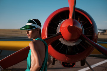 fashion pilot girl in a visor next to propeller plane on the sunset