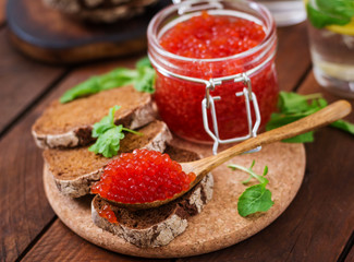 Jar with red caviar and bread on wooden background
