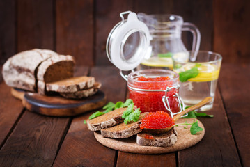 Jar with red caviar and bread on wooden background
