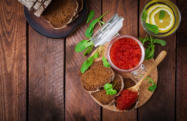 Jar with red caviar and bread on wooden background. Flat lay. Top view