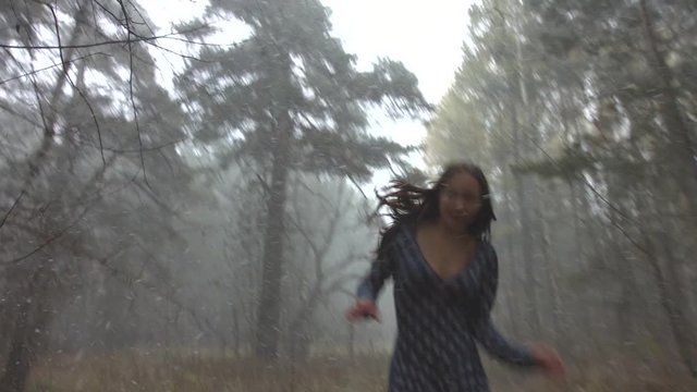 Young girl in fear running through the woods.

Snowfall in the gloomy autumn forest. Beautiful girl is afraid and runs away. Slow motion.