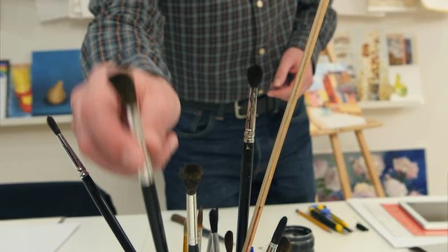 Man artist selecting paintbrushes of different sizes