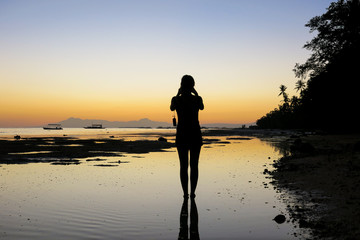Fototapeta na wymiar Woman Taking Sunset Pictures on Beach
