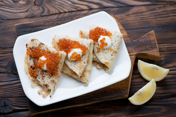 Crepes with red caviar and sour cream in a rustic wooden setting