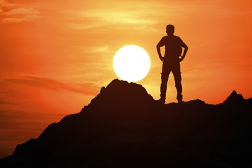 Silhouette of young man standing on the top of the mountain with beautiful sunset background, concept for success and victory.