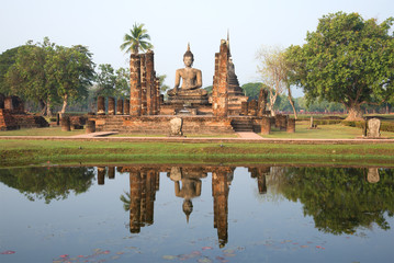 Fototapeta na wymiar Ancient sculpture of the sitting Buddha on ruins of the Buddhist temple early in the morning. Historical park of the Sukhothai, Thailand