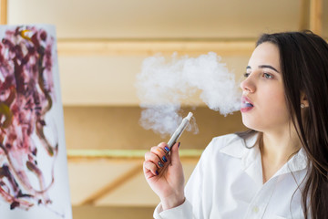 young female smoker smoking e-cigarette outdoors. Head and shoulders, side view