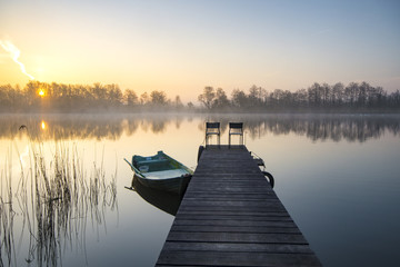 boat moored to a wooden bridge, a beautiful sunrise over the lak