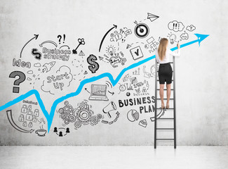 Rear view of a blond woman drawing a sketch and a blue graph on a concrete wall while standing on a...