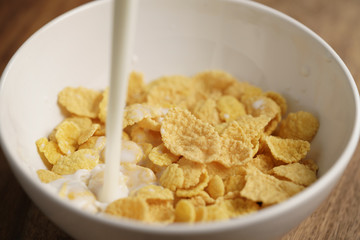 milk pour into bowl with corn flakes, preparing breakfast