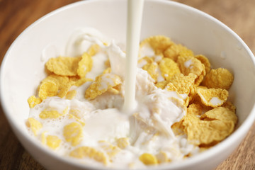 milk pour into bowl with corn flakes, preparing breakfast