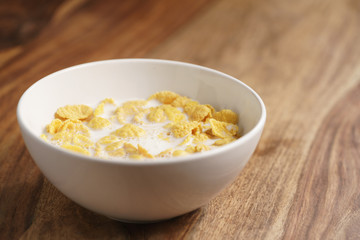corn flakes with milk in white bowl on wood table, simple healthy breakfast
