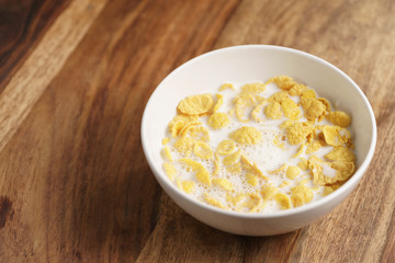 corn flakes with milk in white bowl on wood table, simple healthy breakfast