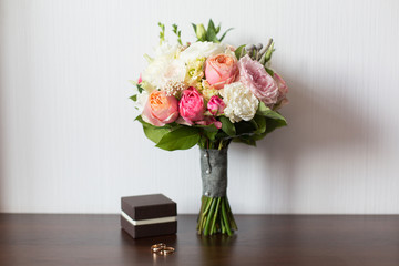 Wedding bouquet and delicate little brown box with wedding rings on a wooden surface