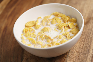 corn flakes with milk in white bowl on wood table, simple healthy breakfast