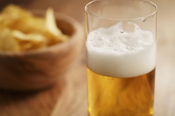 glass of lager beer with potato chips on wooden table, focus on beer