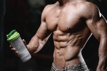 Handsome athletic fitness man holding a shaker and posing gym
