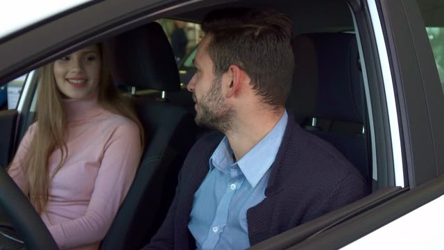 Nice young couple talking inside the car at the dealership. Attractive caucasian man and woman looking at each other. Brunette bearded guy disscusing new car with his girlfriend