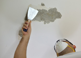 Man scraping a ceiling with a plaster spatula, preparing it for smoothing