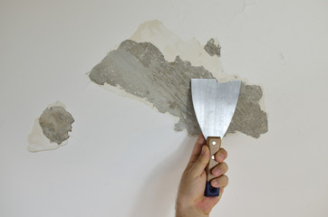 Hand holding a plaster spatula, peeling a ceiling, preparing it for smoothing