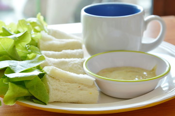 roll bread stuffed bologna and green oak with coffee cup on plate