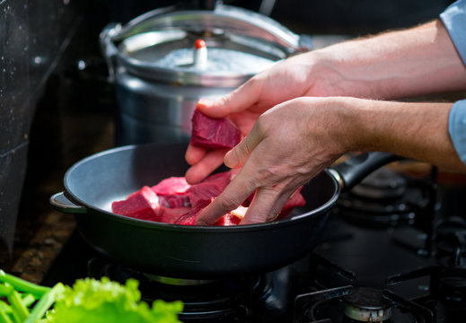 Male hands put the meat in a frying pan