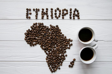 Map of the Ethiopia made of roasted coffee beans laying on white wooden textured background with two coffee cups and space for text