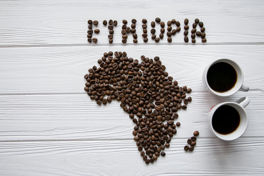 Map of the Ethiopia made of roasted coffee beans laying on white wooden textured background with two cups of coffee and space for text