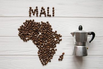 Map of the Africa made of roasted coffee beans and coffee maker on white wooden textured background with space for text