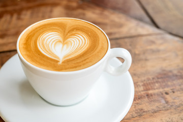 Close up white coffee cup with heart shape latte art on wood tab