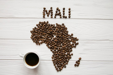 Map of the Africa made of roasted coffee beans and cup of coffee on white wooden textured background with space for text