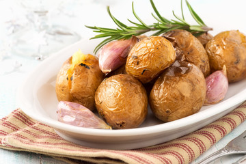Oven baked potatoes or jacket potatoes with rosemary and garlic cloves on a white plate