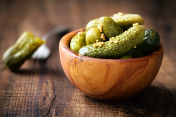 Pickled cucumbers in a wodden bowl wih mustard seeds against dark rustic background