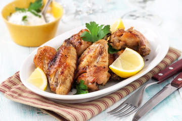 Grilled chicken wings with lemon slices and parsley on a white oval plate