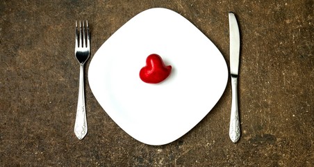 Festive table setting for Valentines Day or Wedding with a fork, knife and hearts on a dark wooden table. The view from the top.