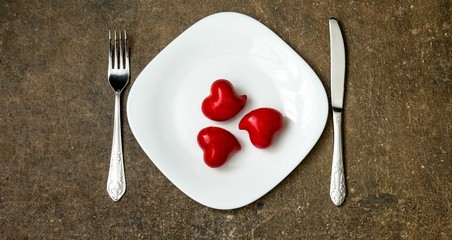 Festive table setting for Valentines Day or Wedding with a fork, knife and hearts on a dark wooden table. The view from the top.