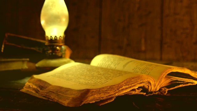 Old books and vintage oil lamp. Kerosene lantern and open old book on wooden table. 4K UHD video footage. Ultra high definition 3840X2160