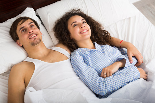 Young people lounging in bed with open eyes