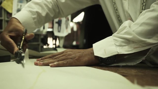 Bespoke tailor working at a factory, making chalk lines and cutting fabric for a suit