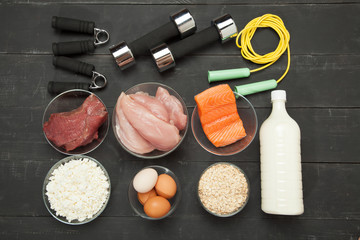 Proteins and dumbbells. Fish, cheese, eggs, meat, chicken  heart on a black wooden background
