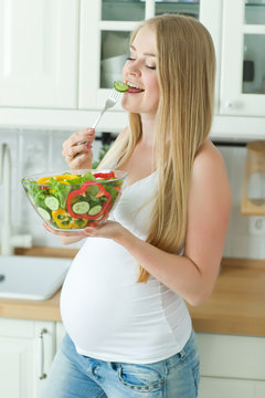 Pregnant woman holding glass bowl with fresh salad 