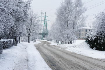 Road in winter forest covered with snow and electric wire towers on a background. 