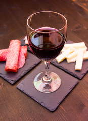 Slices of salami and wine on slate plates on a wooden table seen up close