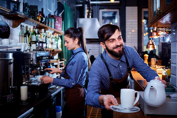 Bartender waiter with a kettle and mug of coffee tea working in the workplace bar, cafe.