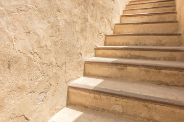 An adobe flight of stairs against a plaster wall of the courtyard of a traditional Arabian house.
