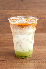 Iced matcha and espresso latte in plastic glass on wooden background