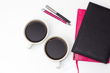 Fototapeta na wymiar two cups of black coffee, two of the diary and two pens on a white background. flat lay of the business concept of relationship men and women