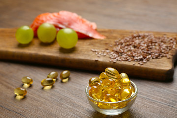 Fish oil pills, flax grain, grape and fish fillet on wooden background