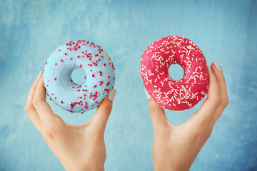 Female hands holding tasty donuts on color background