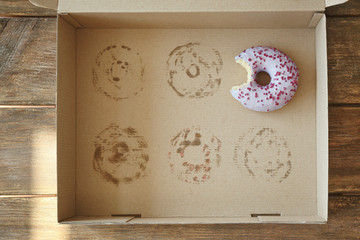 Donut with bite taken out lying in carton box